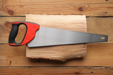Photo of Saw with colorful handle and log on wooden background, top view