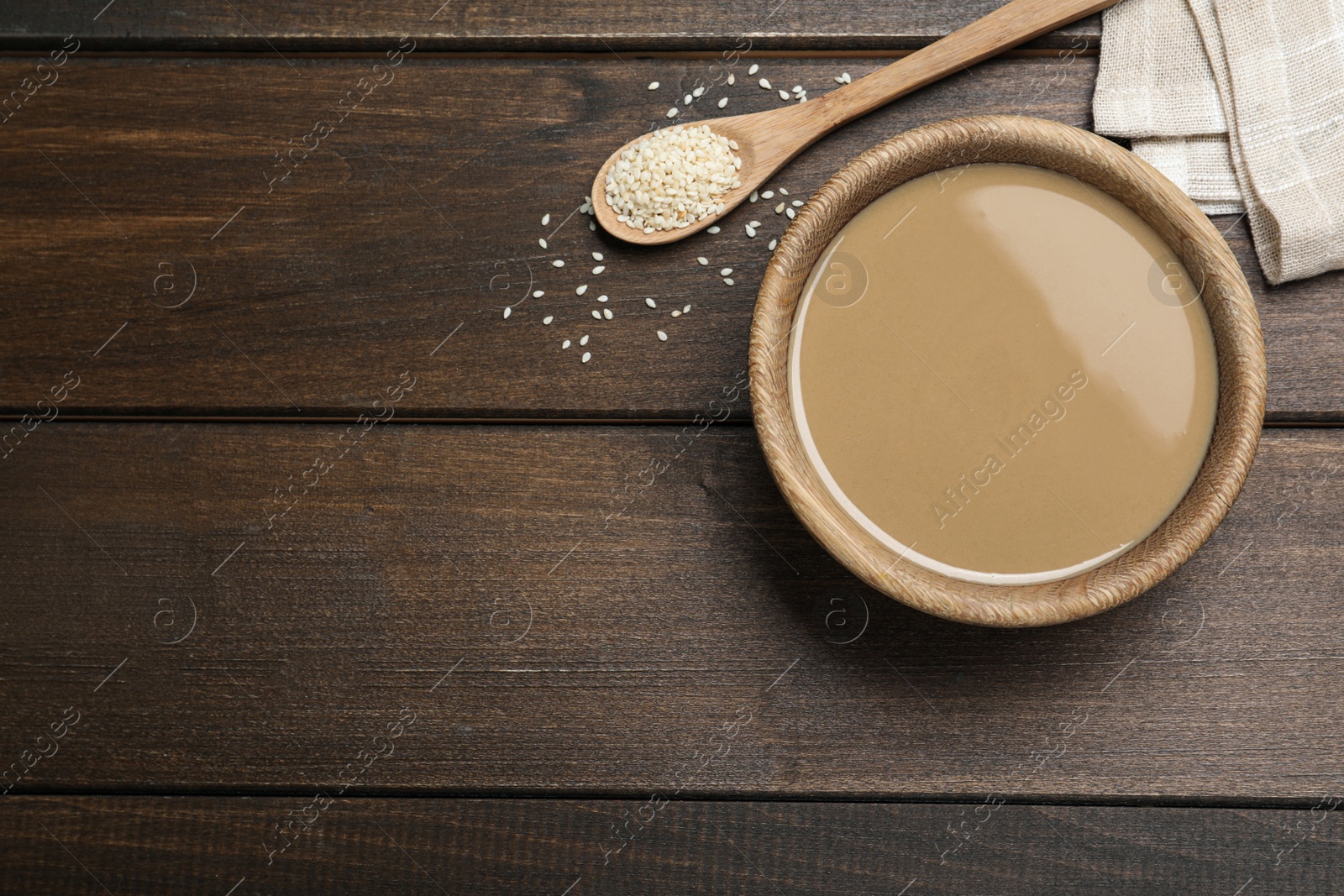 Photo of Tasty sesame paste, seeds and spoon on wooden table, flat lay. Space for text