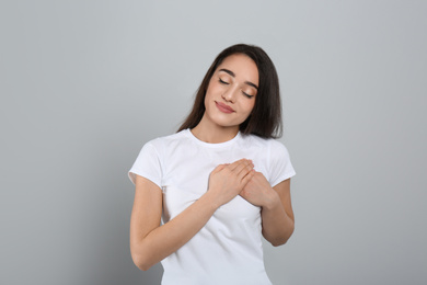 Photo of Beautiful grateful woman with hands on chest against light grey background