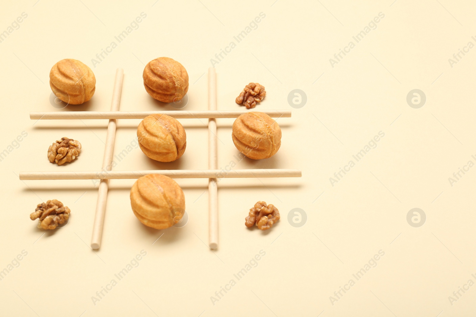 Photo of Tic tac toe game made with walnuts and cookies on beige background. Space for text