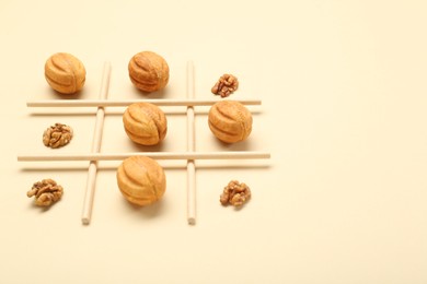 Photo of Tic tac toe game made with walnuts and cookies on beige background. Space for text