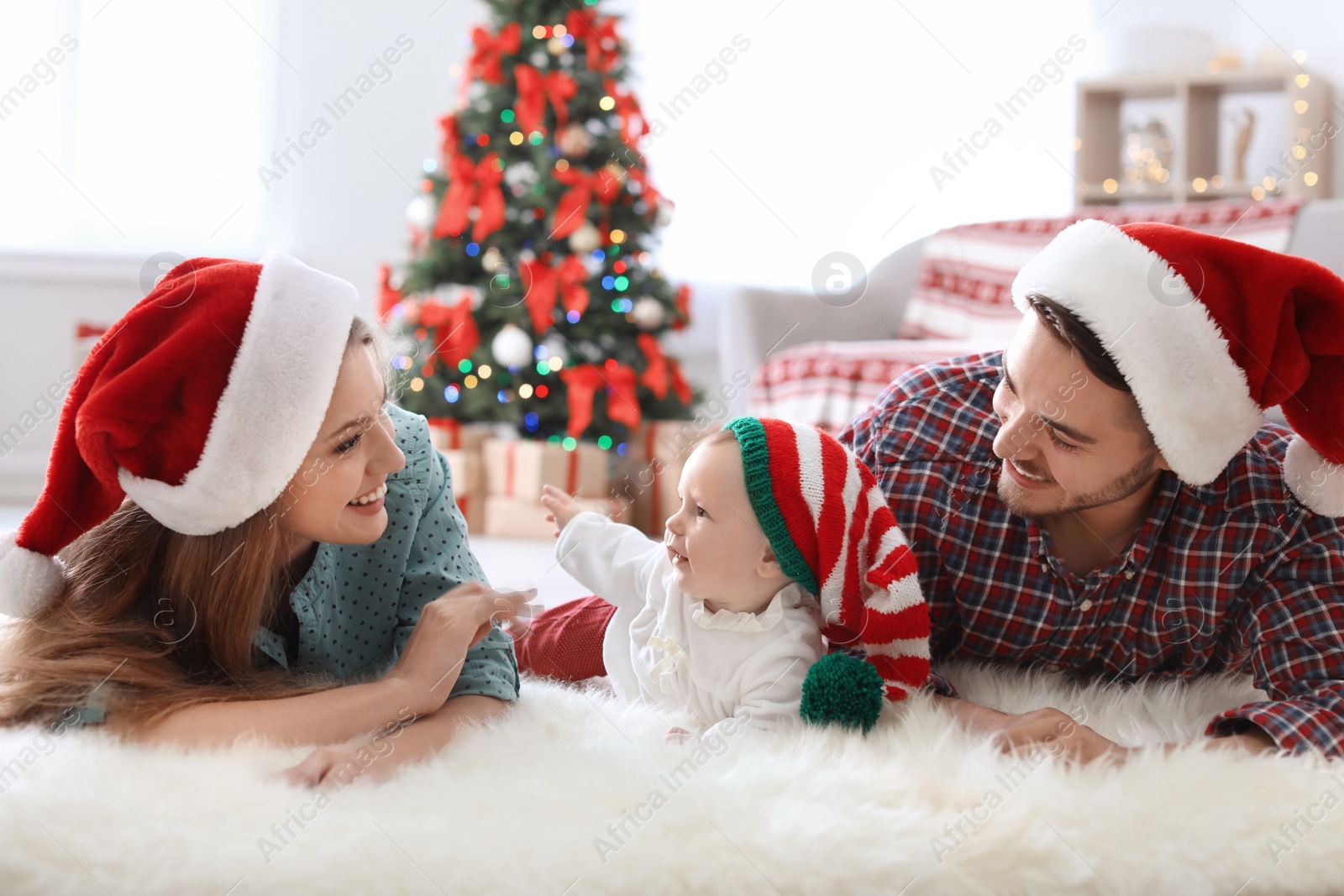 Photo of Happy couple with baby in Christmas hats at home