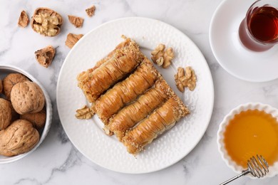 Photo of Eastern sweets. Pieces of tasty baklava, walnuts and tea on white marble table, flat lay