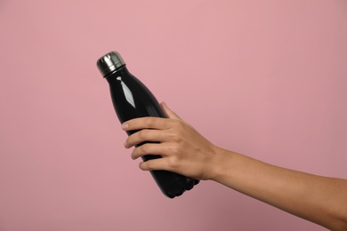 Woman holding modern dark thermos on pink background, closeup