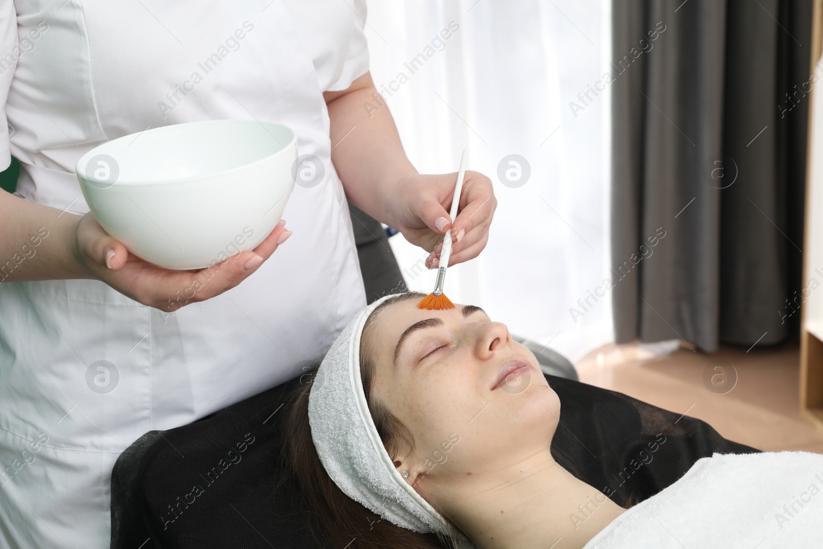 Photo of Cosmetologist with brush applying cosmetic product to client`s face in clinic, closeup