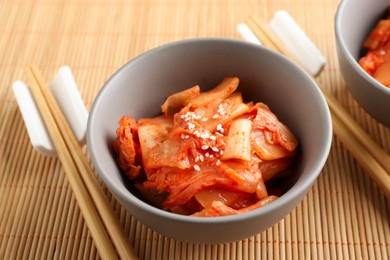 Bowls of spicy cabbage kimchi and chopsticks on bamboo mat, closeup