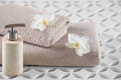 Photo of Soft folded towels, orchid flowers and dispenser on white table