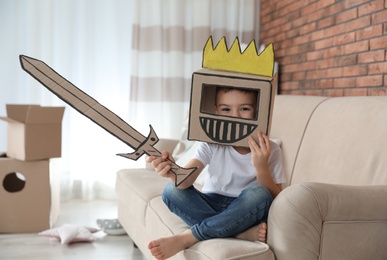 Photo of Cute little boy wearing cardboard armor in living room