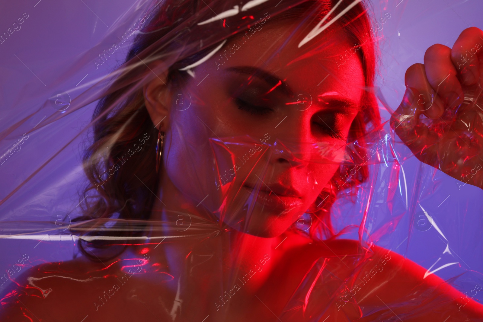 Photo of Fashionable portrait in neon lights. Beautiful young woman posing through transparent film, closeup