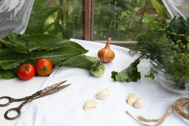 Photo of Fresh green herbs, tomatoes, garlic cloves, onion, scissors and twine on table indoors