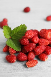 Pile of wild strawberries and leaves on white wooden table, closeup