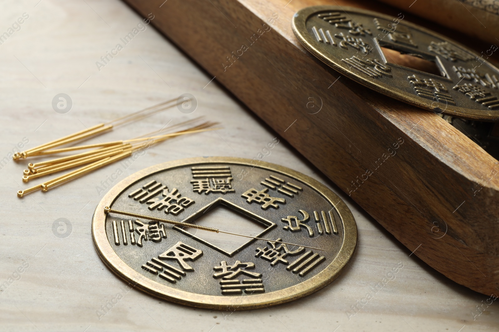 Photo of Acupuncture needles and Chinese coins on beige marble table, closeup