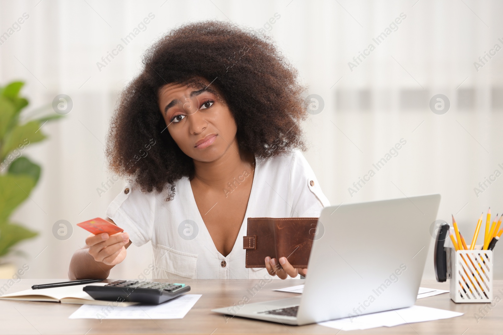 Photo of Confused woman with credit card and wallet planning budget at table indoors. Debt problem