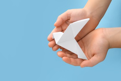 Photo of Origami art. Child holding paper bird on light blue background, top view. Space for text