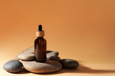 Photo of Bottle of face serum and spa stones on beige background, space for text