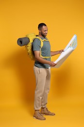 Photo of Happy tourist with backpack and map on yellow background