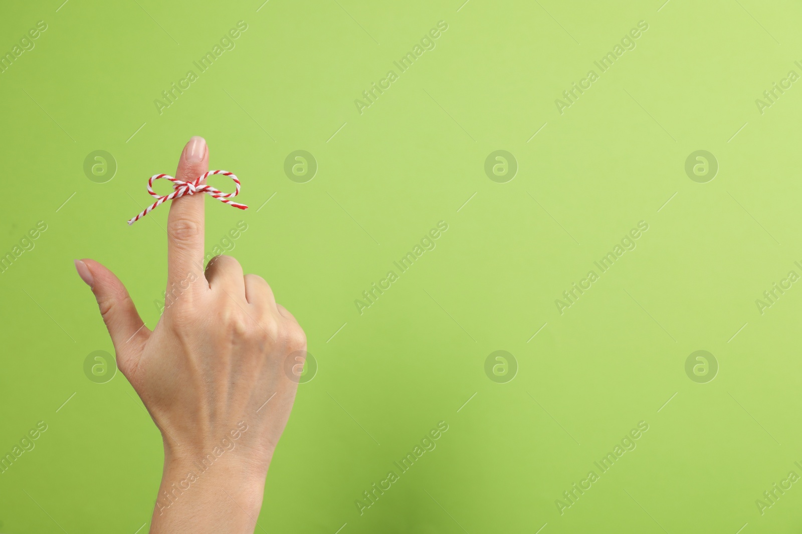 Photo of Woman showing index finger with tied bow as reminder on light green background, closeup. Space for text