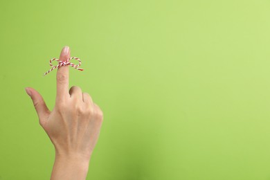 Woman showing index finger with tied bow as reminder on light green background, closeup. Space for text