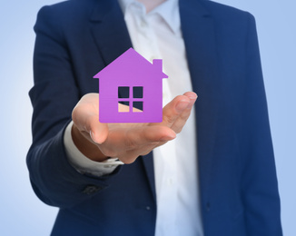 Image of Home security concept. Woman holding house on light background, closeup