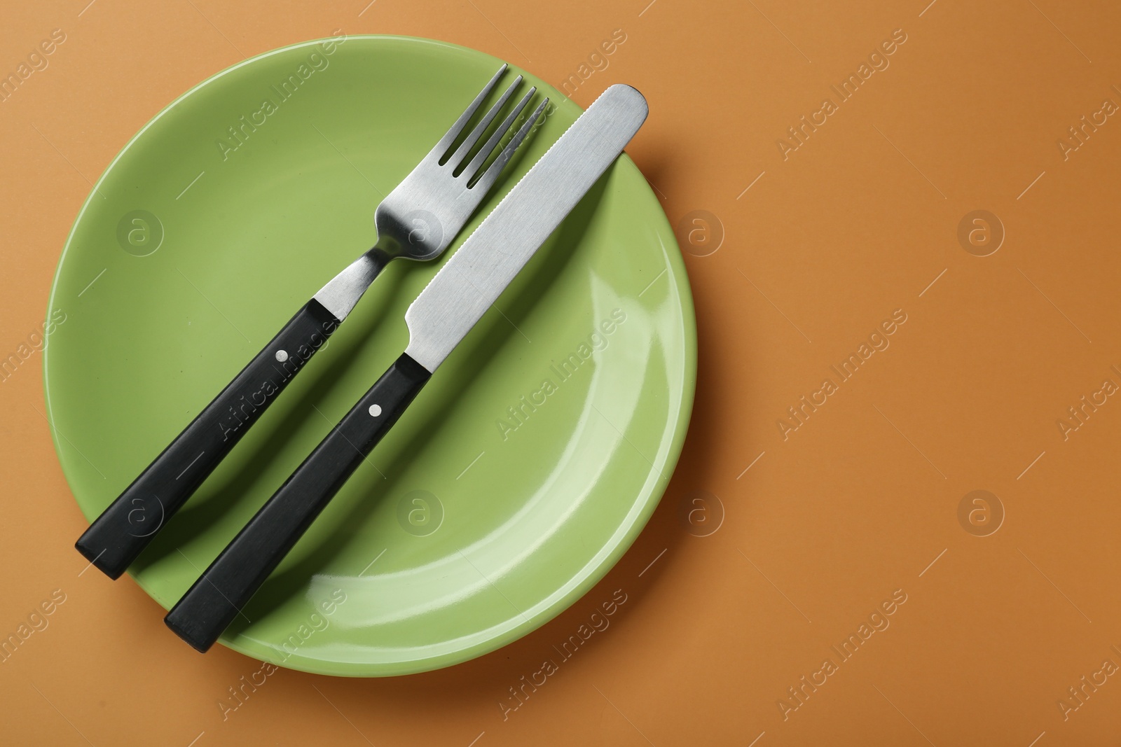 Photo of Green ceramic plate with cutlery on pale orange background, top view. Space for text