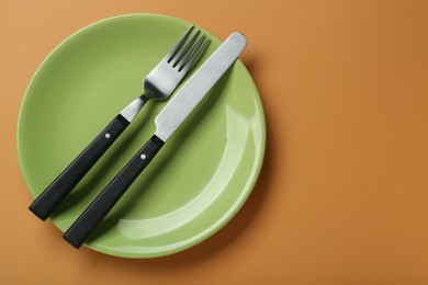 Photo of Green ceramic plate with cutlery on pale orange background, top view. Space for text