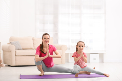 Photo of Young mother with little daughter practicing yoga at home