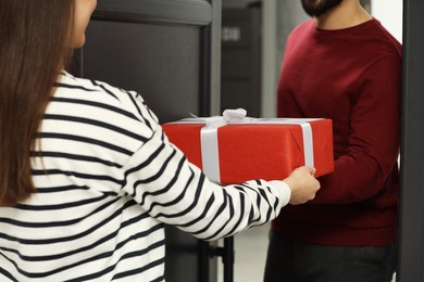 Photo of Courier giving young woman Christmas gift box indoors, closeup. Sending present by mail