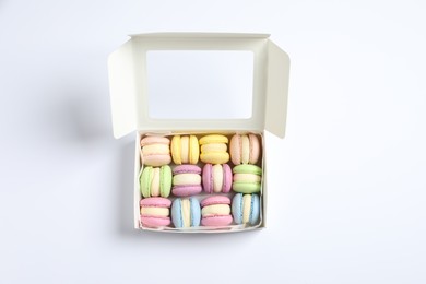 Photo of Many delicious colorful macarons in box on white background, top view