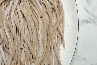 Photo of Uncooked homemade soba (buckwheat noodles) on white marble table, top view