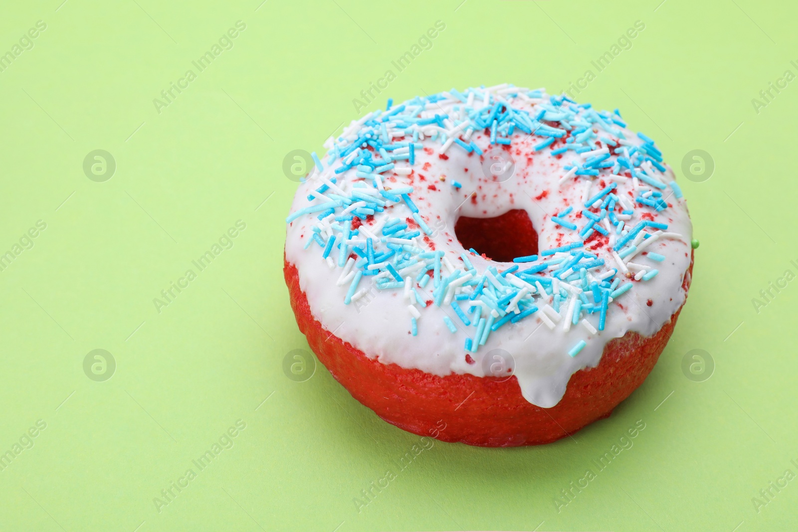 Photo of Glazed donut decorated with sprinkles on green background, closeup. Space for text. Tasty confectionery