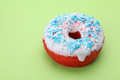 Glazed donut decorated with sprinkles on green background, closeup. Space for text. Tasty confectionery