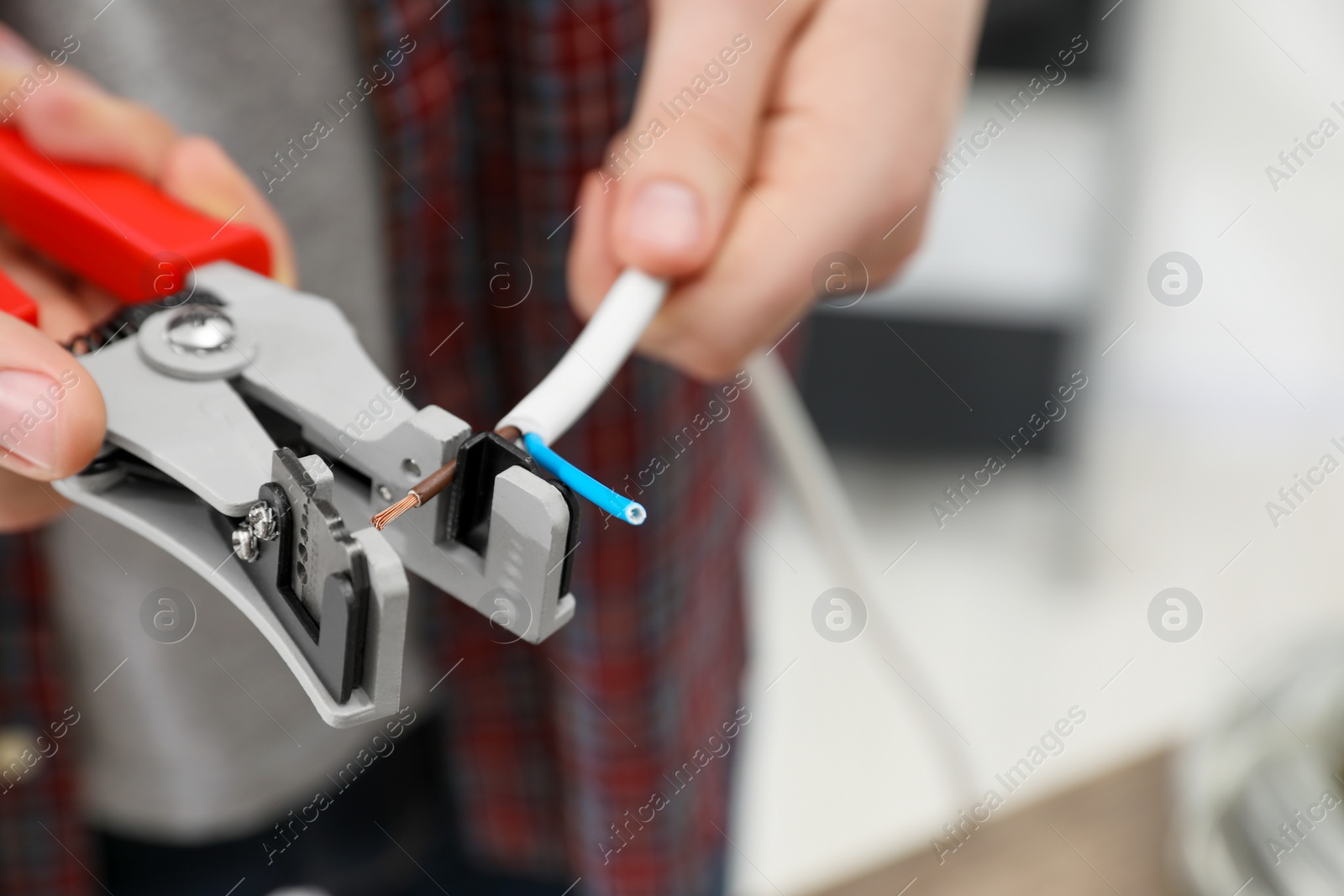 Photo of Professional electrician stripping wiring indoors, closeup. Space for text