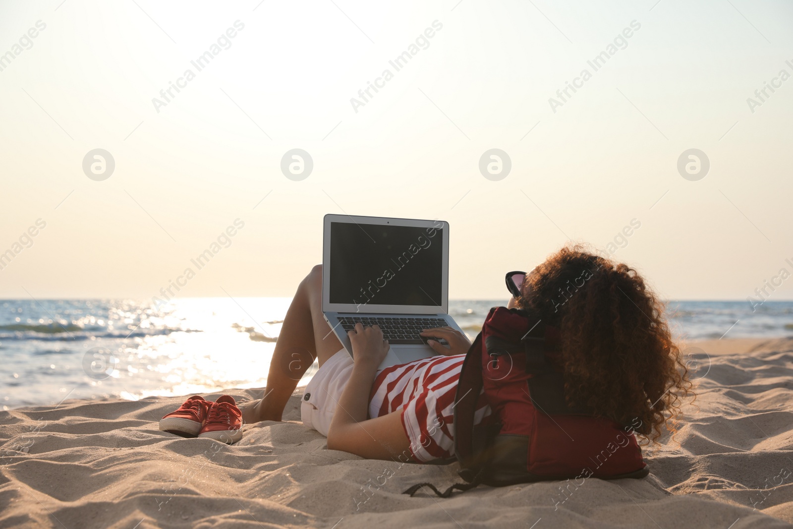 Photo of African American woman working on laptop at beach