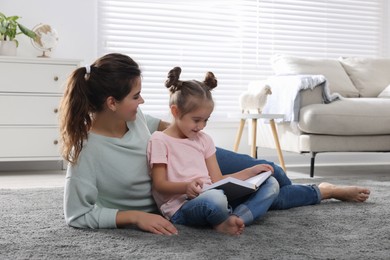 Photo of Young mother and her daughter reading book on floor at home