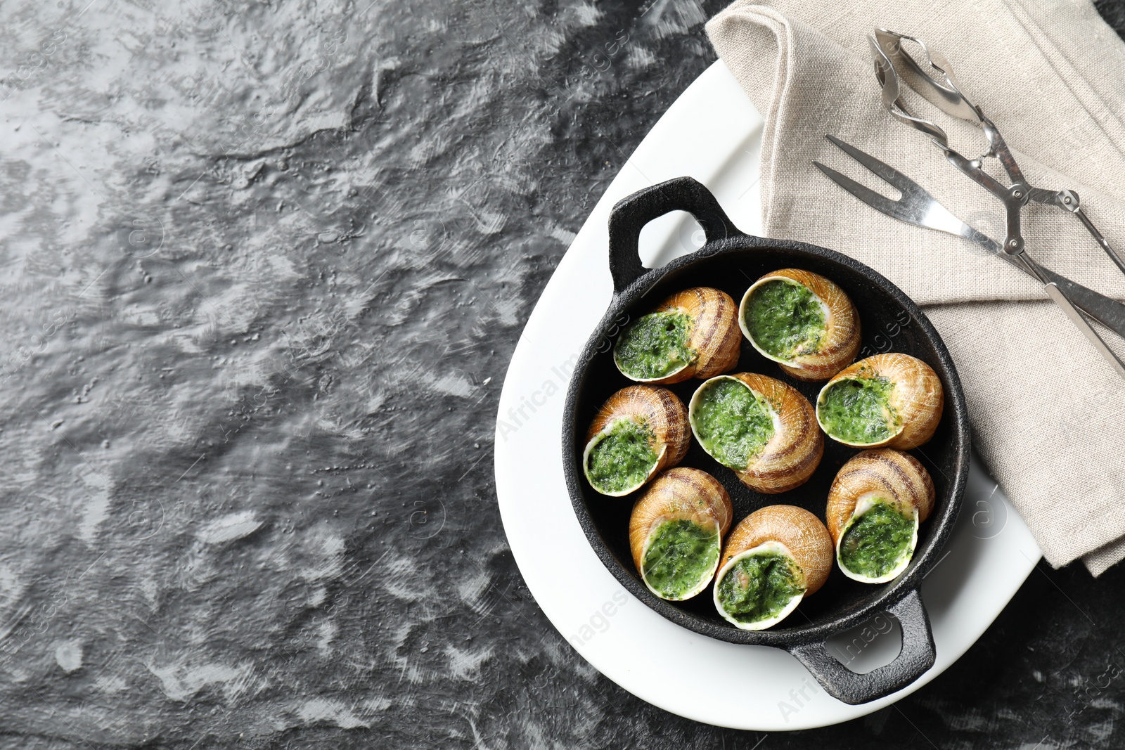 Photo of Delicious cooked snails in baking dish served on grey textured table, flat lay. Space for text