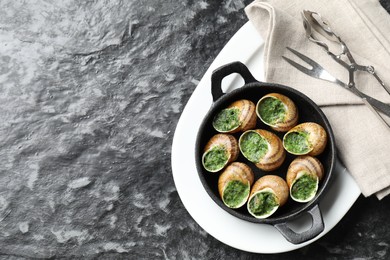 Delicious cooked snails in baking dish served on grey textured table, flat lay. Space for text