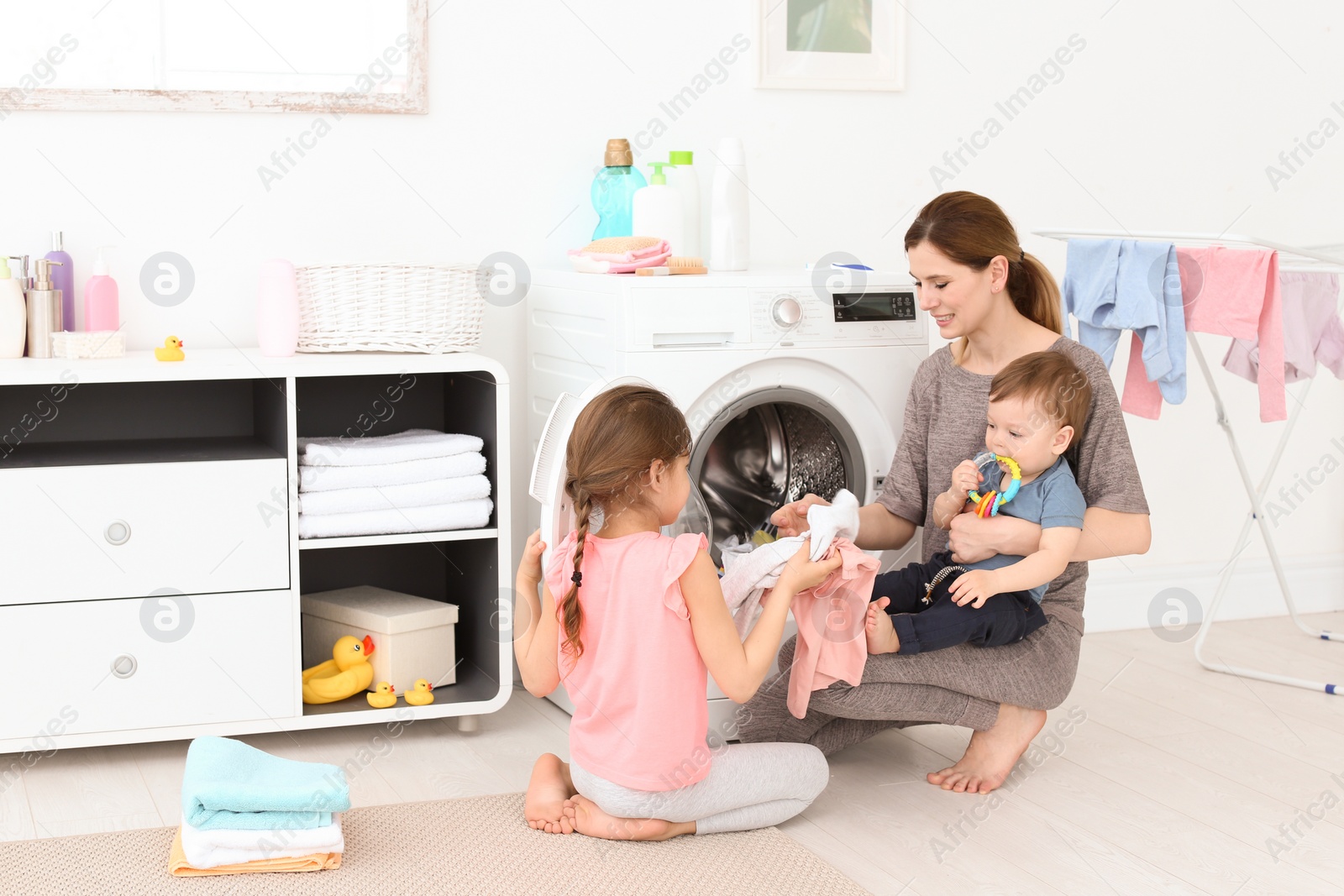 Photo of Housewife with little children doing laundry at home