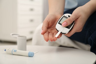 Photo of Diabetes. Woman checking blood sugar level with glucometer at light table, closeup