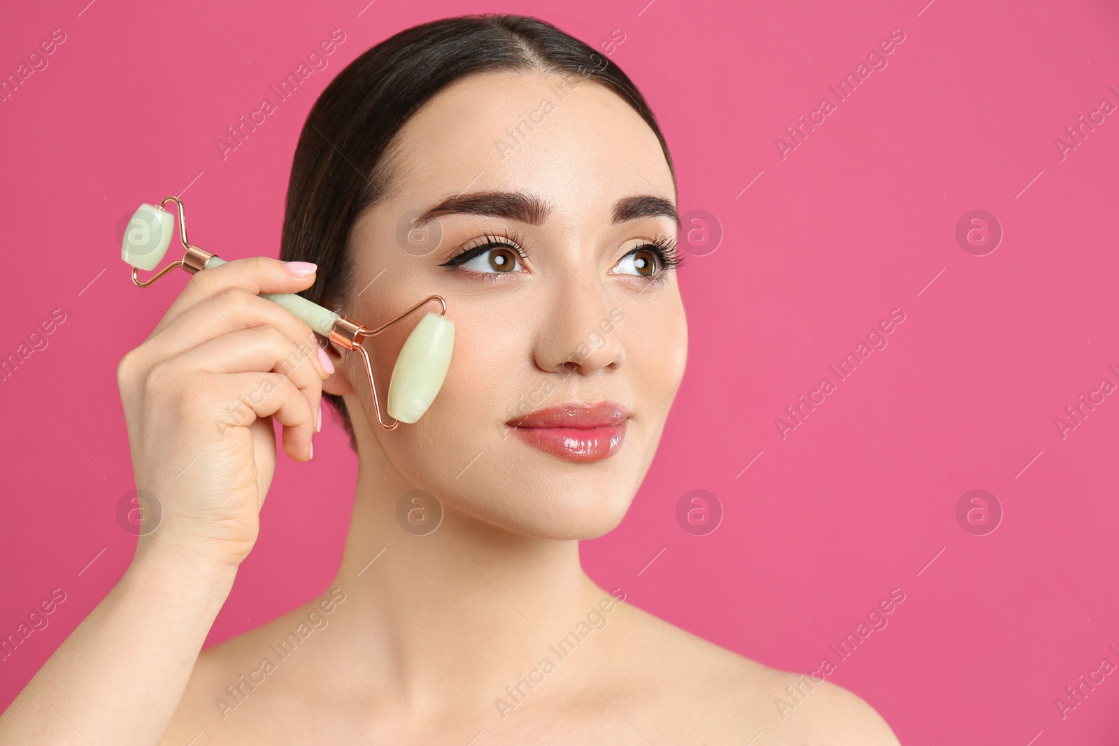 Photo of Woman using natural jade face roller on pink background, space for text