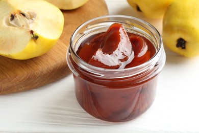 Photo of Tasty homemade quince jam in jar and fruits on white wooden table, closeup