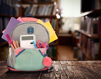 Image of Backpack with school stationery on wooden table in library, space for text