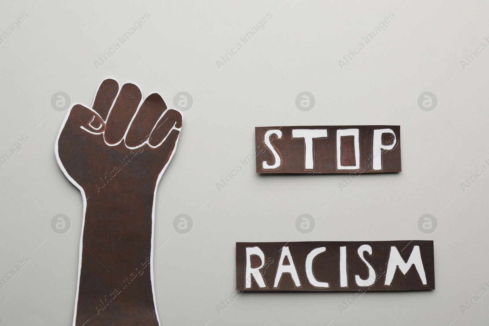 Photo of Phrase Stop Racism near paper hand with clenched fist on light background, flat lay