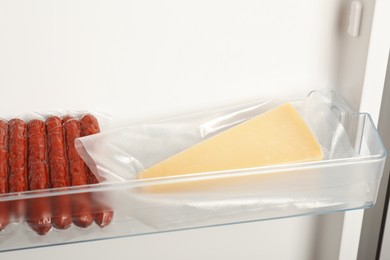 Photo of Vacuum bags with cheese and sausages in fridge. Food storage