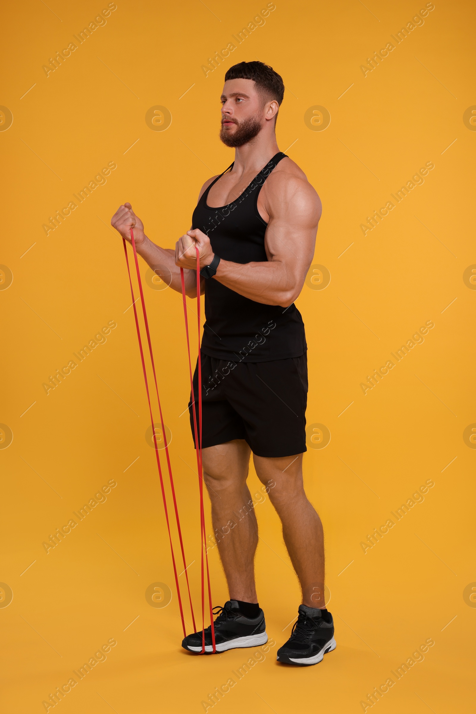 Photo of Young man exercising with elastic resistance band on orange background