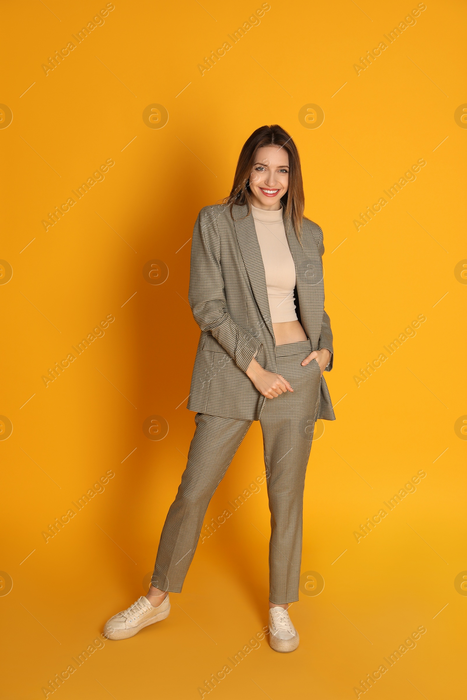 Photo of Full length portrait of beautiful young woman in fashionable suit on yellow background. Business attire