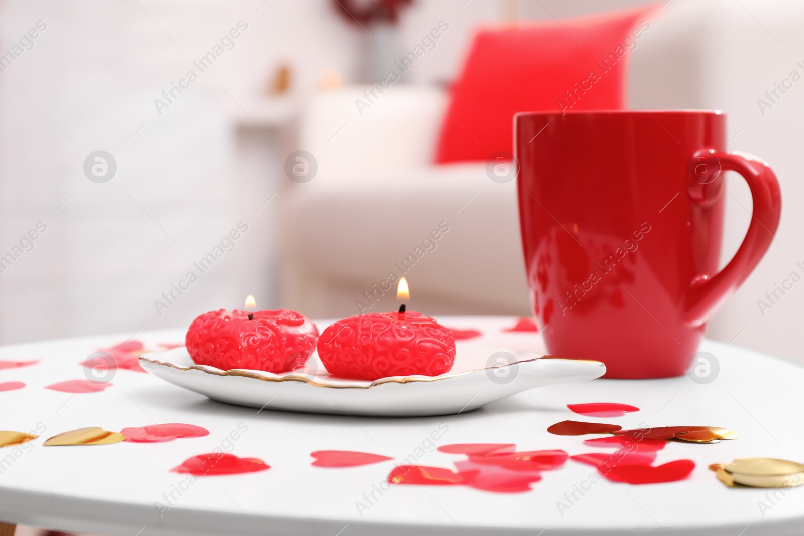 Photo of Red cup, candles and heart shaped confetti on white table indoors. Valentine's Day celebration