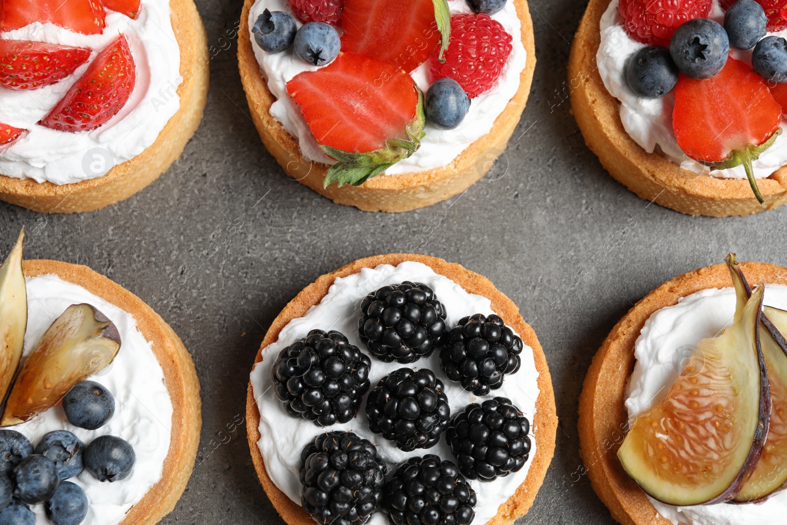 Photo of Different berry tarts on grey table, flat lay. Delicious pastries