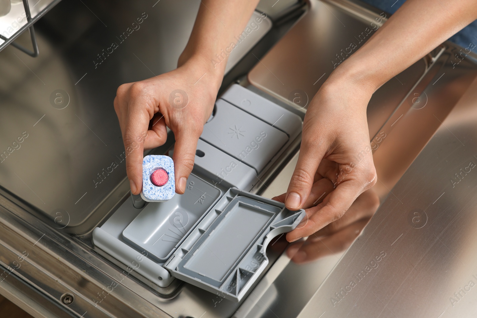 Photo of Woman putting detergent tablet into open dishwasher, closeup