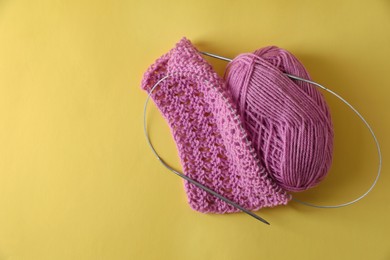 Photo of Pink knitting, yarn and needles on yellow background, top view. Space for text