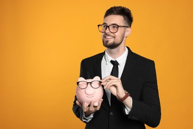 Photo of Happy businessman with piggy bank on orange background. Space for text